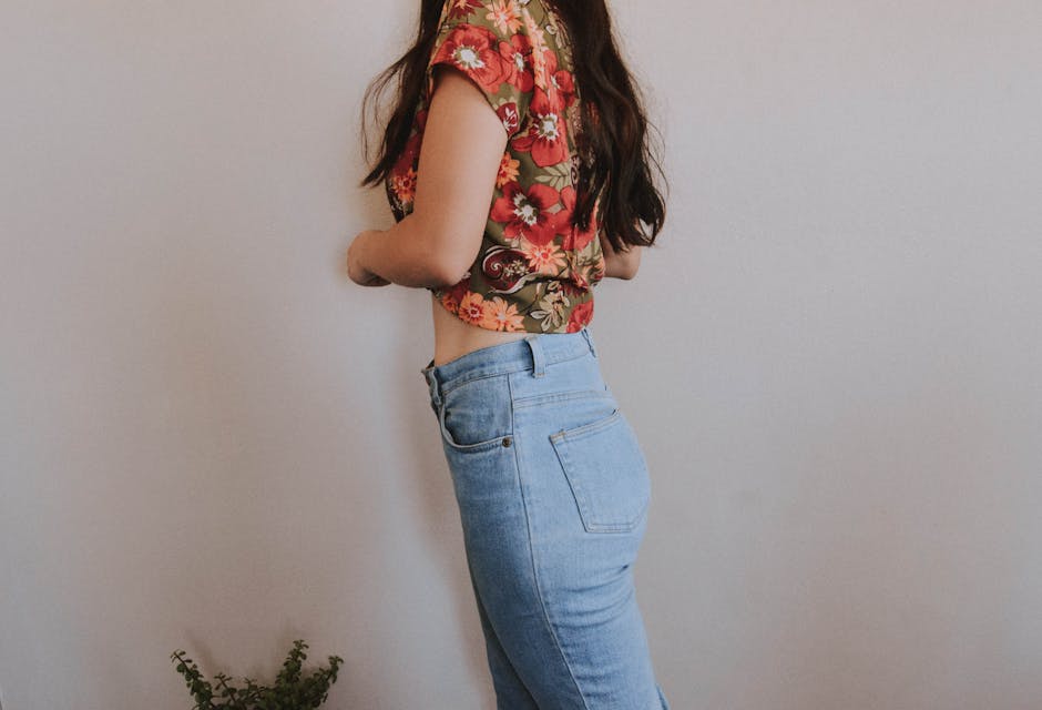 Fashionable woman posing in a floral top and blue jeans inside a minimalistic room.