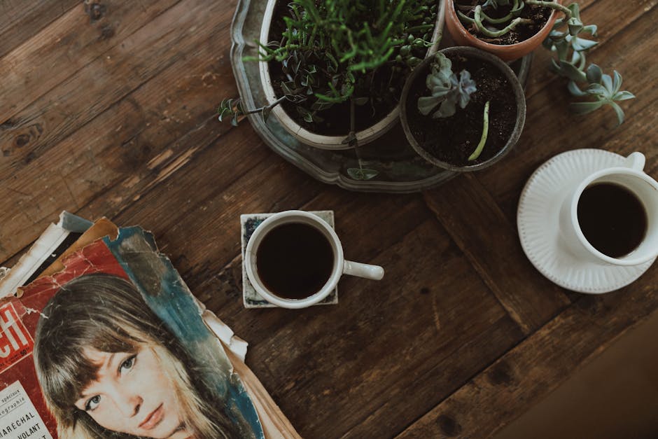 Two cups of coffee with vintage magazines and plants on a rustic table, capturing a cozy atmosphere.