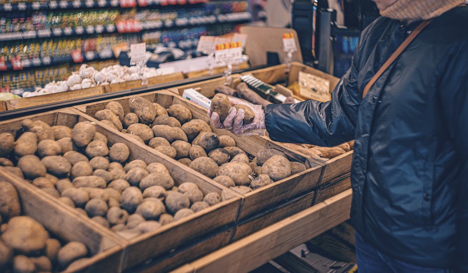 A shopper picks potatoes from a wooden crate in a grocery store produce section.