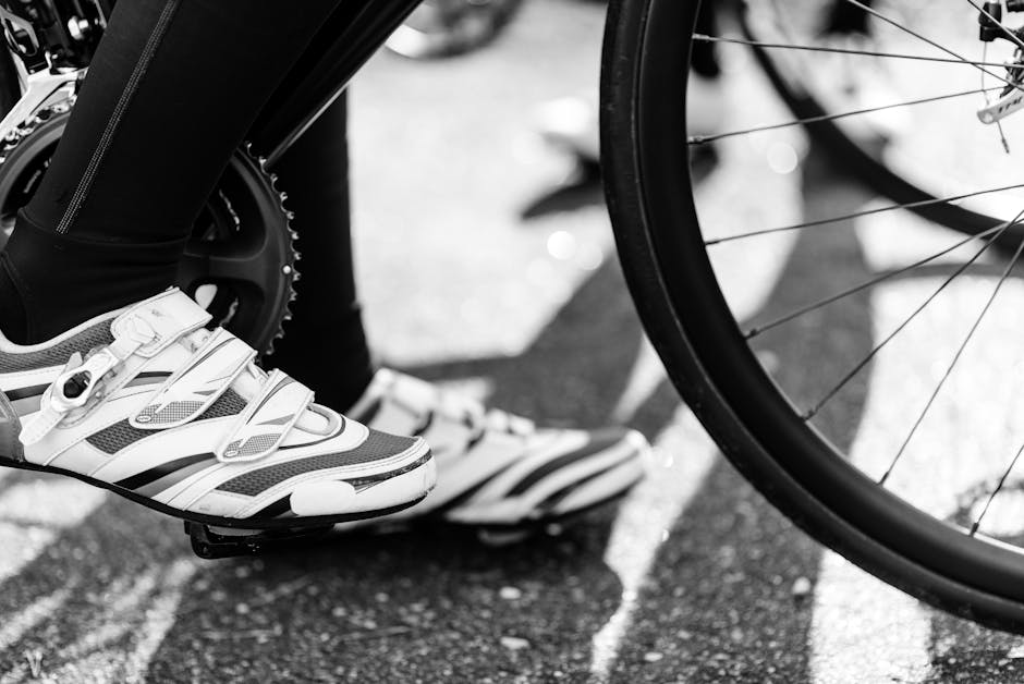 Black and white image showing a cyclist's feet with cleats on a bike pedal, capturing motion and detail.
