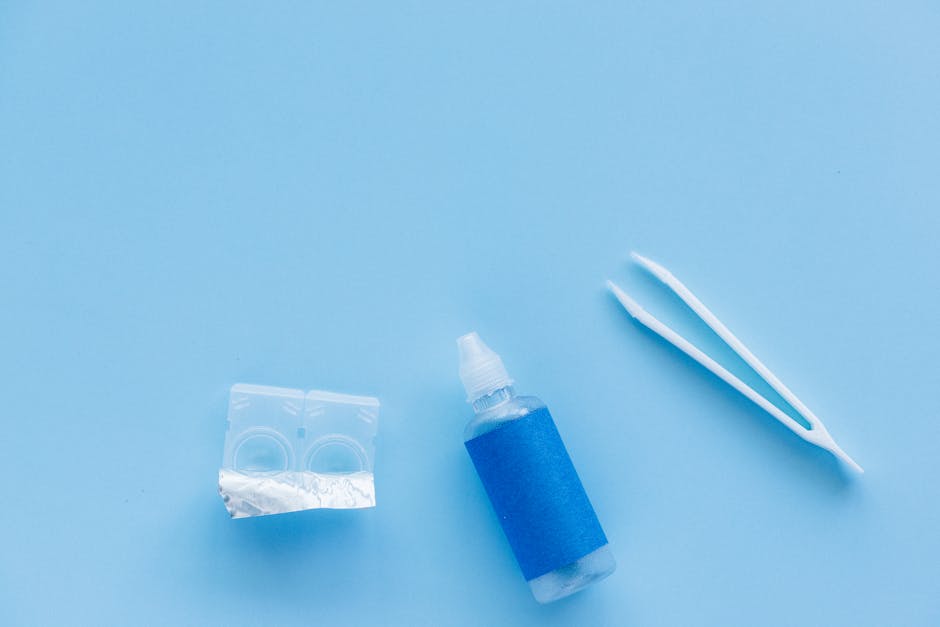 Flat lay of contact lenses, solution bottle, and tweezers on a blue background.