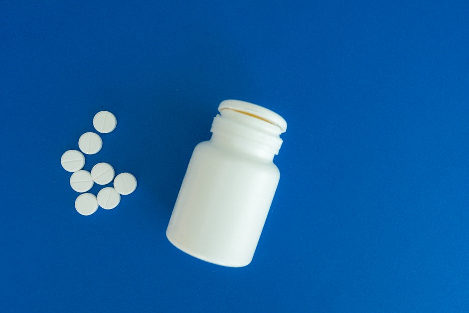 Flat lay of white pills and a container against blue backdrop, symbolizing healthcare.
