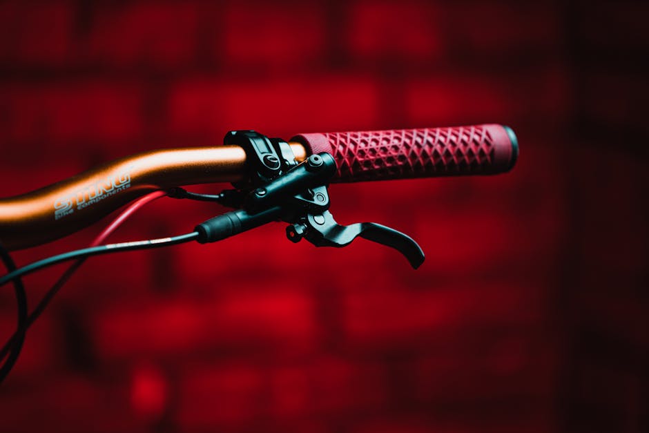 Detailed view of a bicycle handlebar with a red grip. Vivid red backdrop adds contrast.