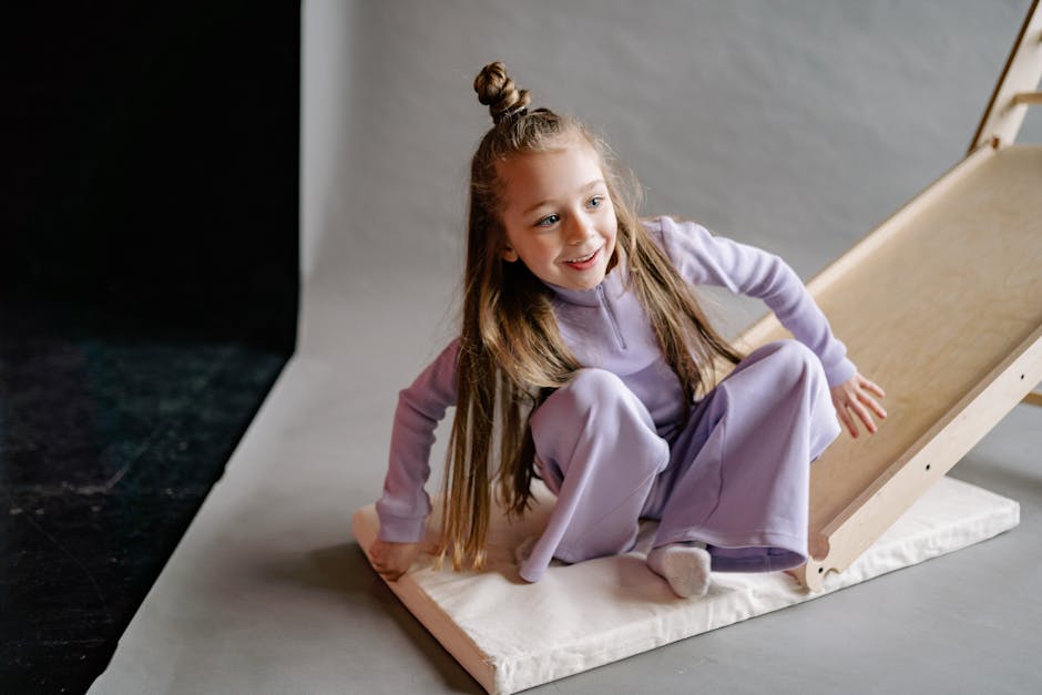 A cheerful girl in a lilac outfit playing on an indoor slide with a joyful expression.