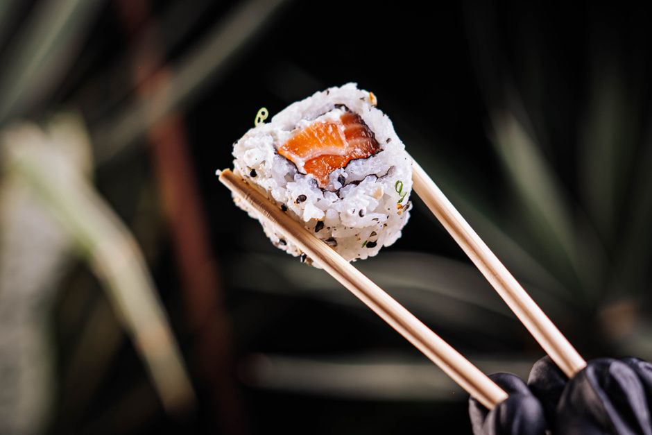 Close-up of a fresh salmon sushi roll held with wooden chopsticks, perfect for culinary blogs.