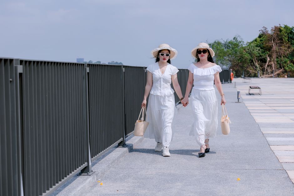 Two women in white summer outfits and sun hats walking outdoors on a sunny day.