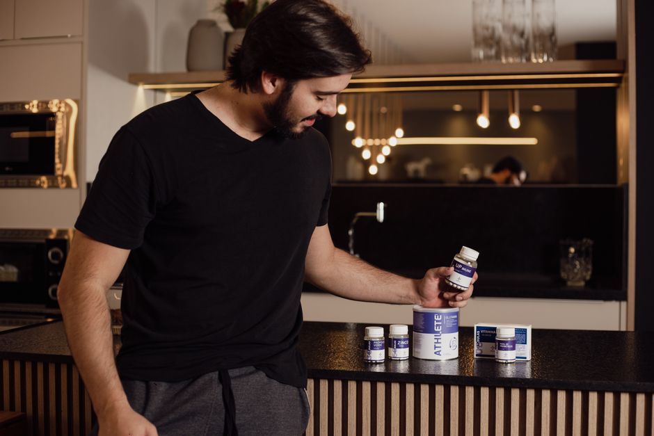 Adult man in modern kitchen examining various health supplements for fitness and wellness.