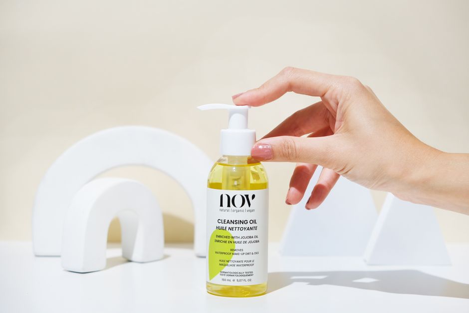 A hand holds a yellow cleansing oil bottle against a minimalist backdrop.