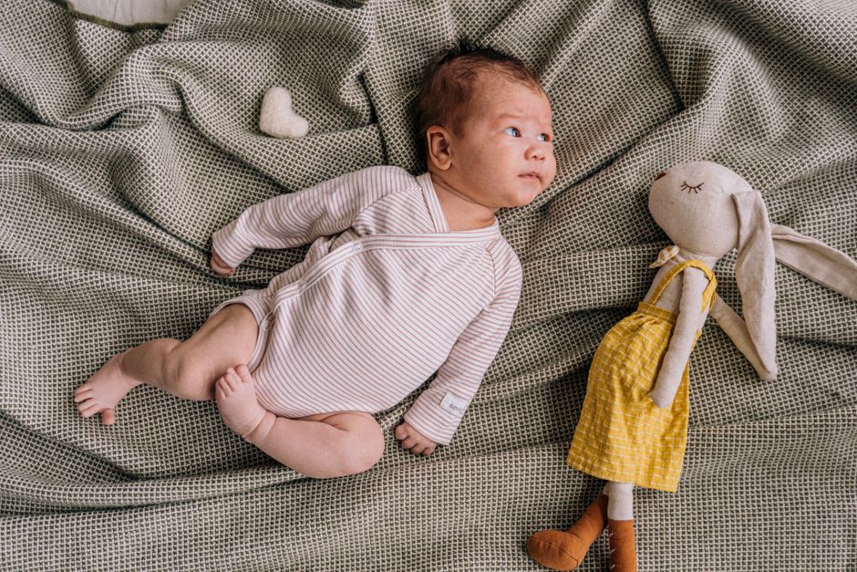 Adorable baby lying on blanket with plush bunny in yellow dress, creating a warm and cozy scene.